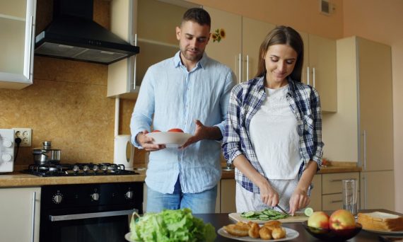 Happy young couple embracing and talking in the kitchen while cooking breakfast at home in the morning