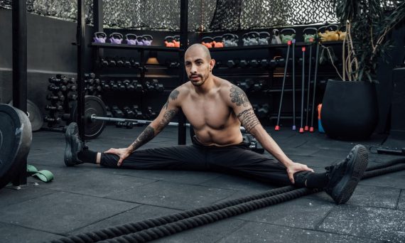 Tattooed man performing a split stretch in a gym, showcasing flexibility and fitness lifestyle in Mexico City.